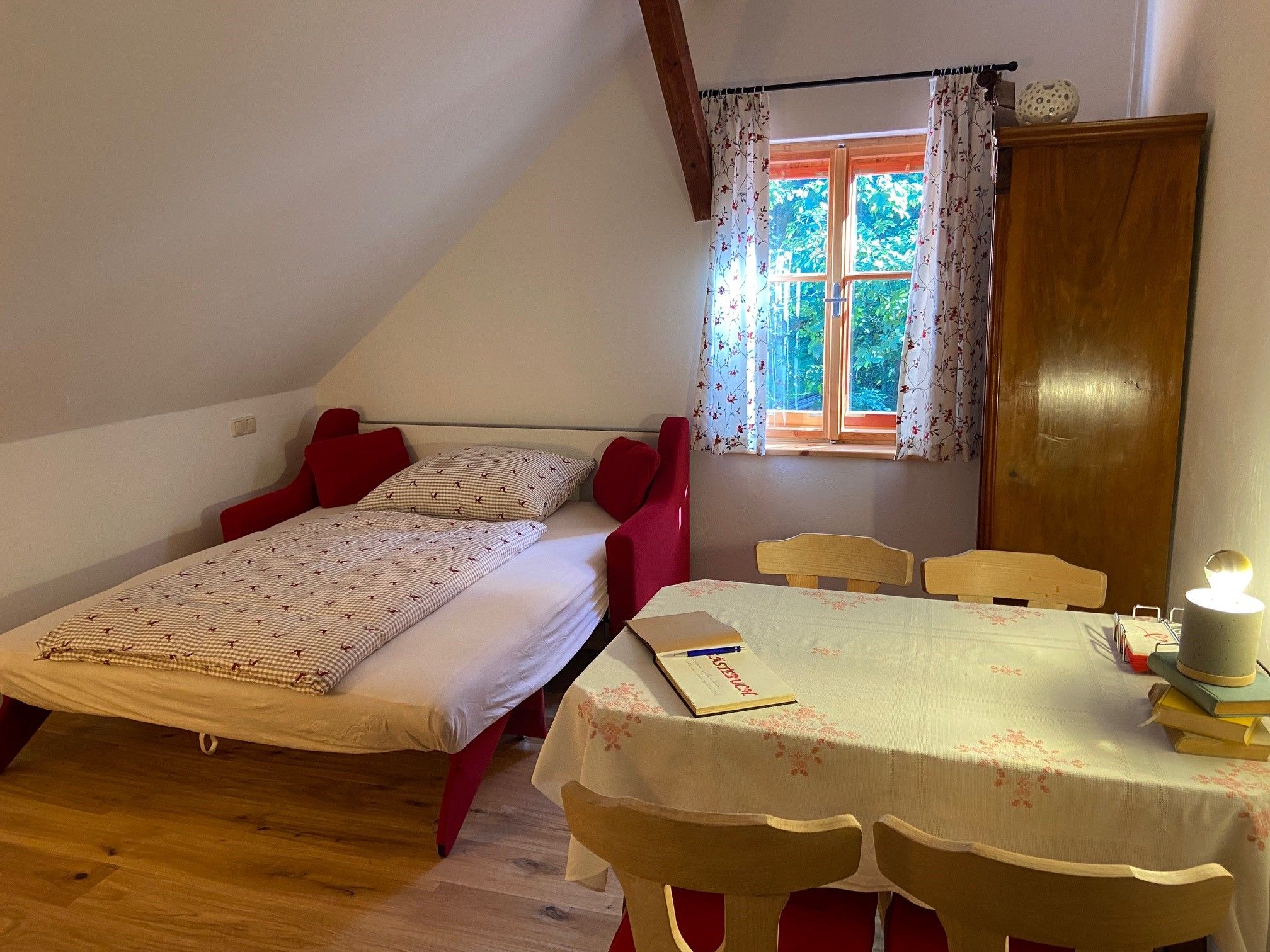 Ein gemütliches Schlafzimmer mit einem Ausziehbett, einem Tisch mit Stühlen und einem Fenster mit Vorhängen.