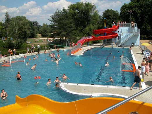 Ein Freibad mit Wasserrutsche und spielenden Menschen.