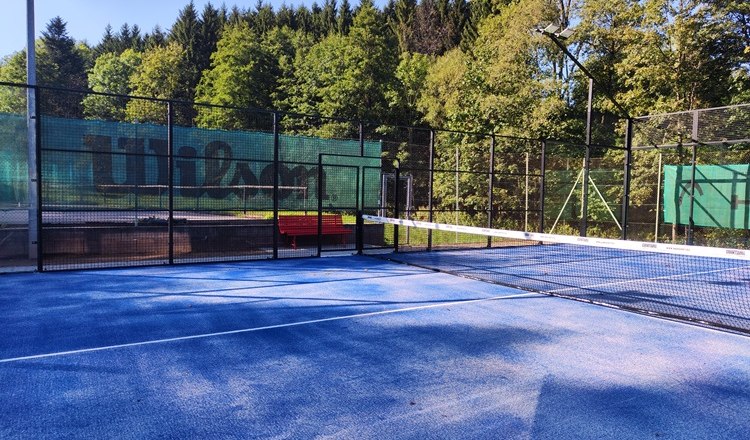 Padelplatz mit blauem Boden und Netz, umgeben von B&auml;umen.