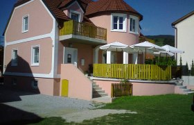 Ein rosa G&auml;stehaus mit Terrasse und Sonnenschirmen.
