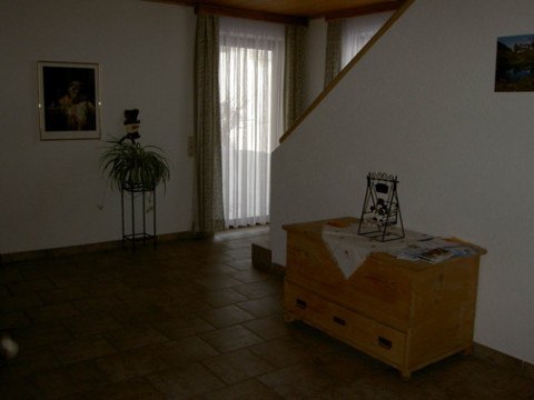 Innenansicht eines Wohnbereichs mit Holzkiste, Pflanze und Treppe.