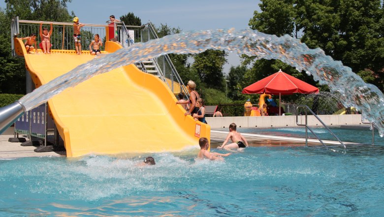 Kinder spielen auf einer gelben Wasserrutsche in einem Freibad.