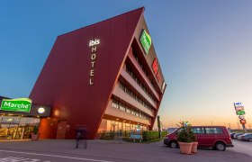 Modernes Hotelgebäude mit schräger Fassade und Leuchtschrift 'ibis HOTEL'.