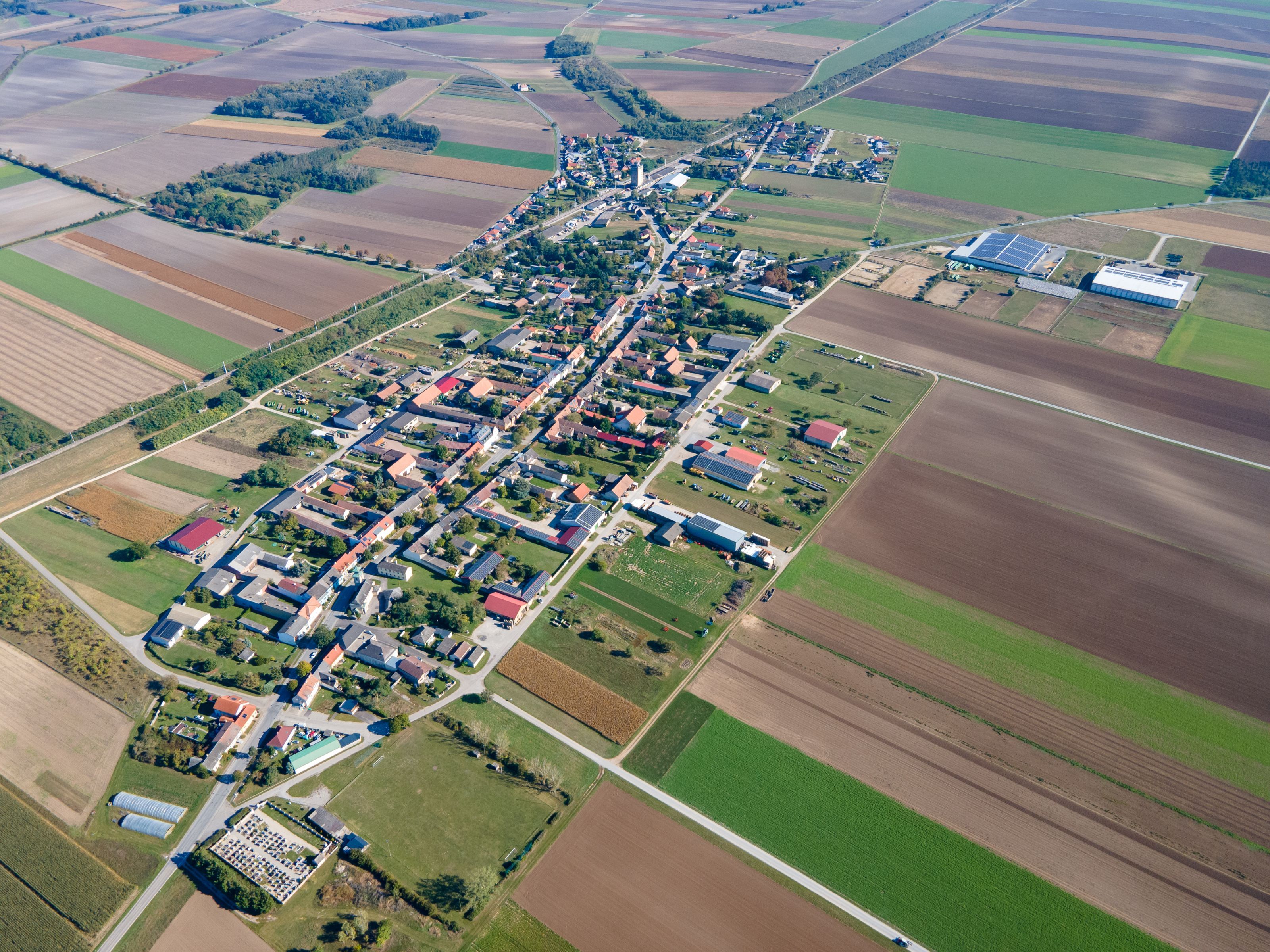 Luftaufnahme der Gemeinde Weiden an der March mit dicht bebautem Ortskern, umgeben von Feldern und landwirtschaftlichen Flächen.