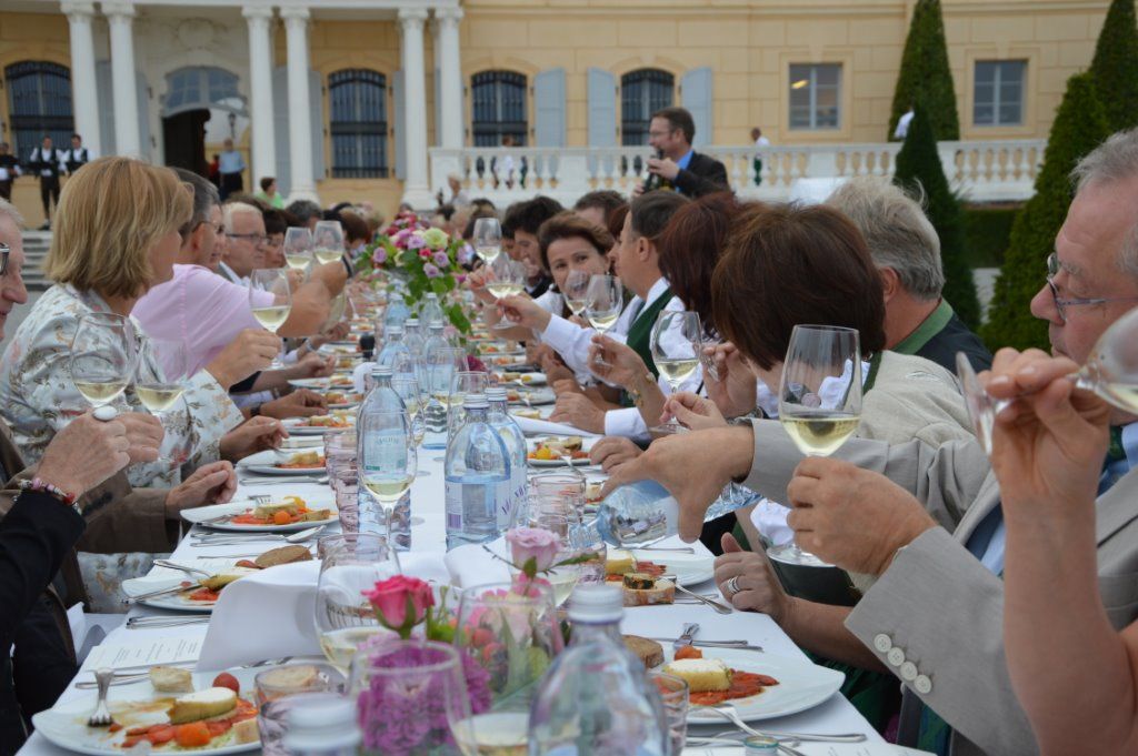 Menschen bei einem festlichen Essen im Freien, mit Wein und gedecktem Tisch.