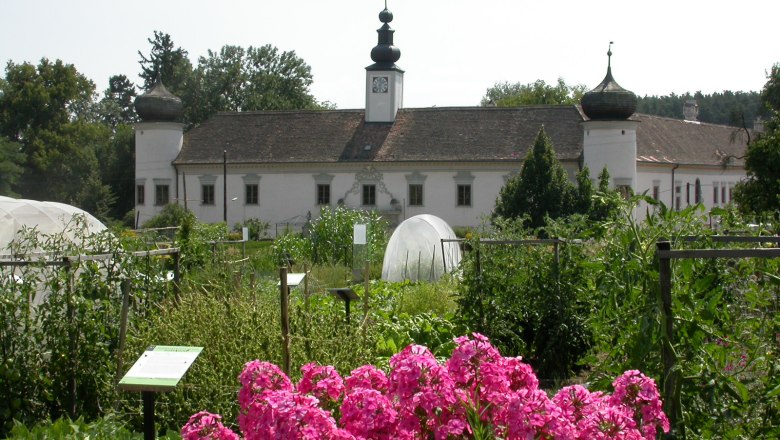 Barockes Geb&auml;ude mit Zwiebelt&uuml;rmen hinter einem bl&uuml;henden Garten.