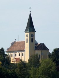 Pfarrkirche Gro&szlig;ebersdorf mit spitzem Turm und Uhr, umgeben von B&auml;umen.