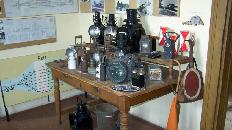 Ein Tisch mit alten Eisenbahnlampen und Signalen in einem Raum mit historischen Pl&auml;nen an der Wand.