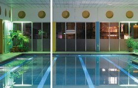 Innenansicht eines beleuchteten Hallenbads mit Schwimmbecken und Pflanzen.