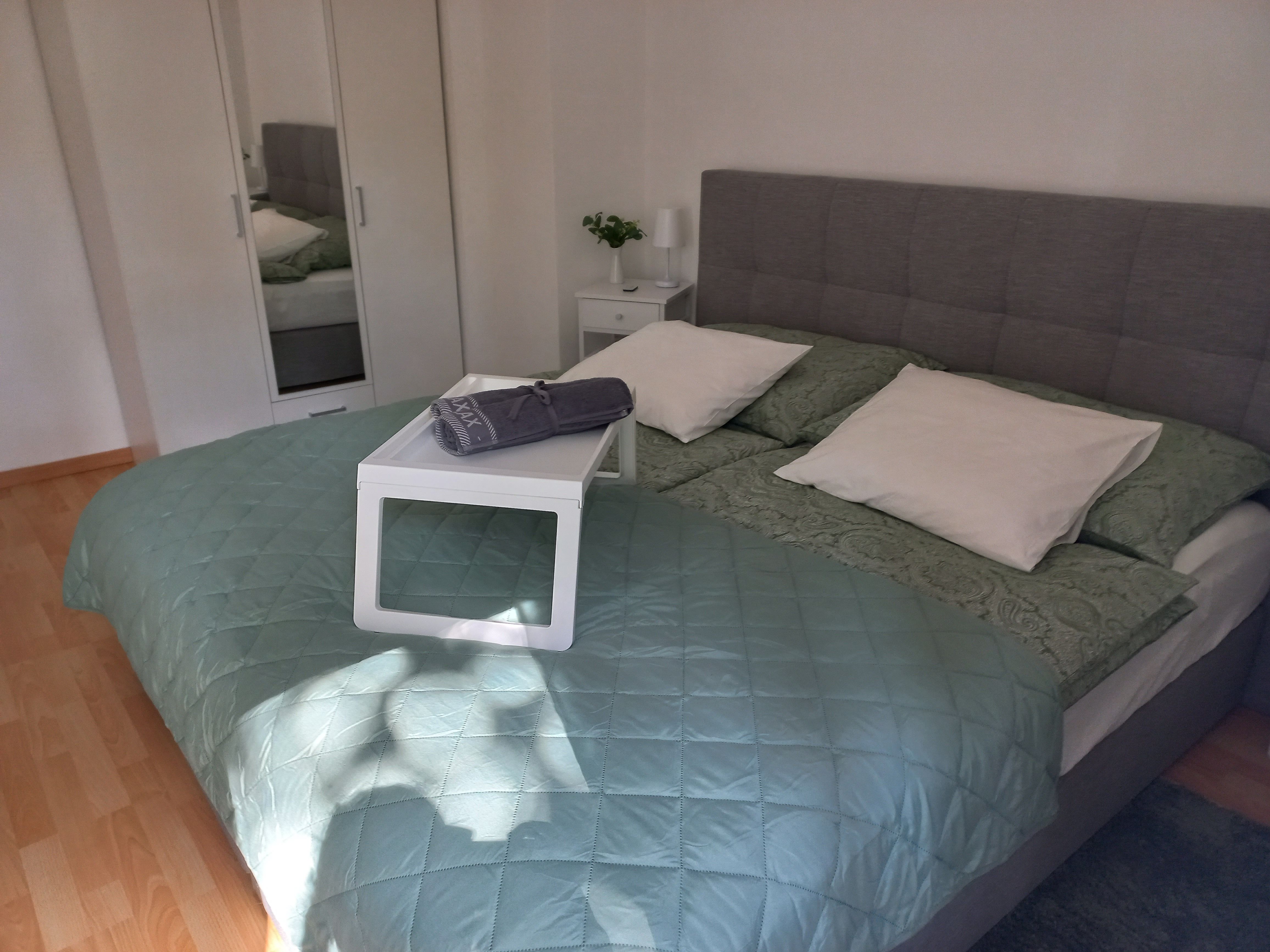 Ein gemütliches Schlafzimmer mit einem großen Bett, grüner Bettdecke und weißen Kissen. Ein Tablett mit Handtuch liegt auf dem Bett.