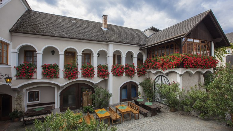 Hausansicht_aussen, © Monika Loeff Traditionelles Gebäude mit Arkaden und Blumenkästen.