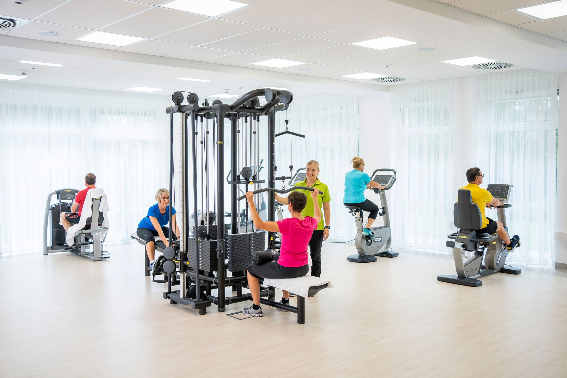 Menschen trainieren in einem hellen Fitnessraum mit verschiedenen Geräten.