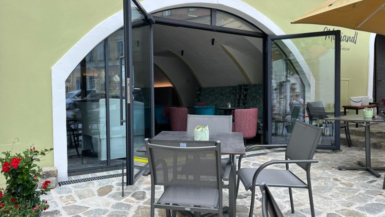 Au&szlig;enansicht eines Caf&eacute;s mit offenen Glast&uuml;ren und Sitzgelegenheiten im Freien.