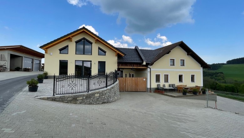 Gelbes Haus mit gro&szlig;en Fenstern auf gepflasterter Fl&auml;che unter blauen Himmel.