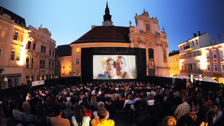 Open-Air-Kinoabend auf einem Platz mit vielen Zuschauern vor einer großen Leinwand.