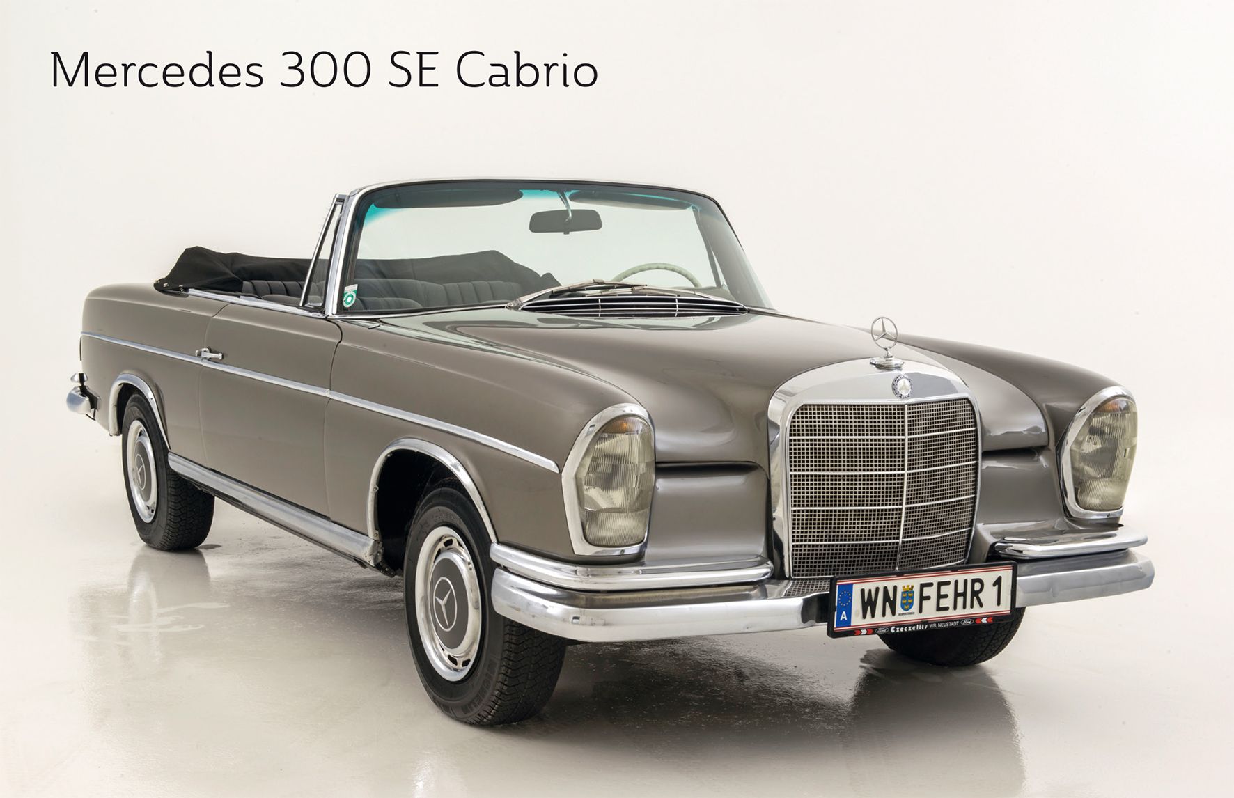 Ein graues Mercedes 300 SE Cabrio mit offenem Verdeck auf weißem Hintergrund.