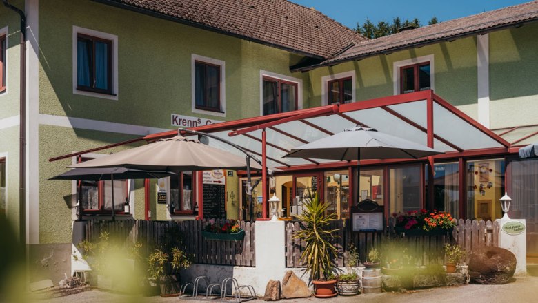 Außenansicht eines Wirtshauses mit Terrasse und Sonnenschirmen.