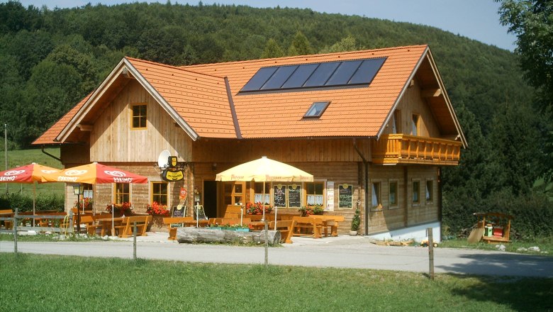 Ein traditionelles Gasthaus mit Holzwänden und roten Dachziegeln, umgeben von grüner Landschaft und Wald.