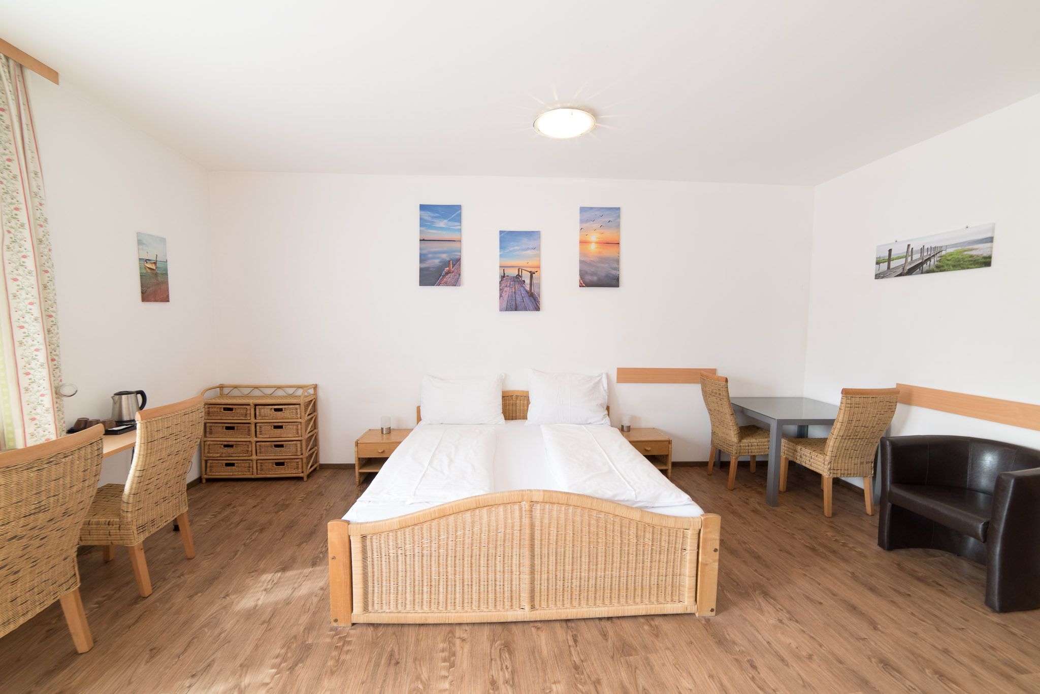 Großes Schlafzimmer mit hellen, beigen Tönen und Rattanmöbel. Sitzmöglichkeit, Schreibtisch, Doppelbett, Couch, Nachtkästchen.