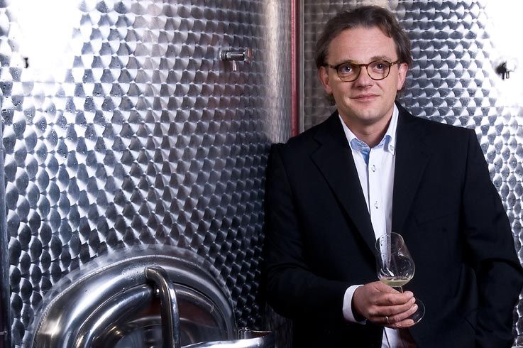 Ein Mann in Anzug hält ein Weinglas vor einem großen Edelstahltank.