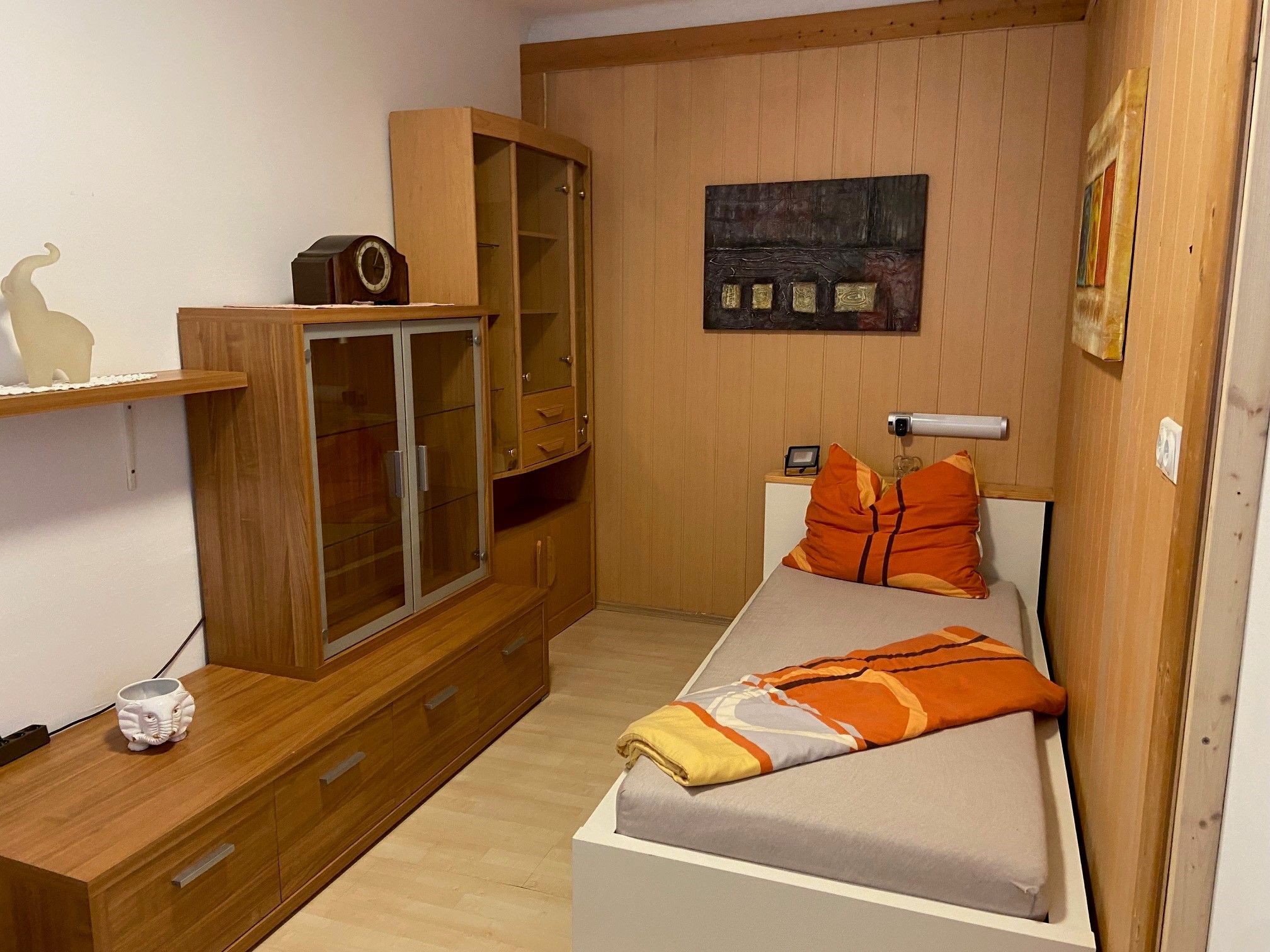 Einzelzimmer mit Holzmöbeln, Einzelbett und Dekoration.