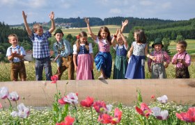Kinder in traditioneller Kleidung stehen auf einem Feld mit Mohnblumen.