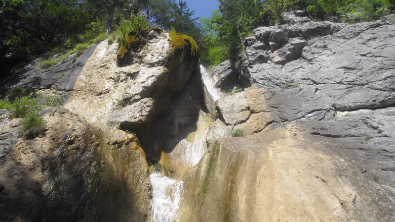 Wasserfall in felsiger Landschaft mit B&auml;umen und blauem Himmel.