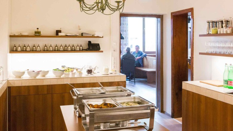 Buffetraum mit Speisen und Blick in ein angrenzendes Zimmer mit zwei Personen.