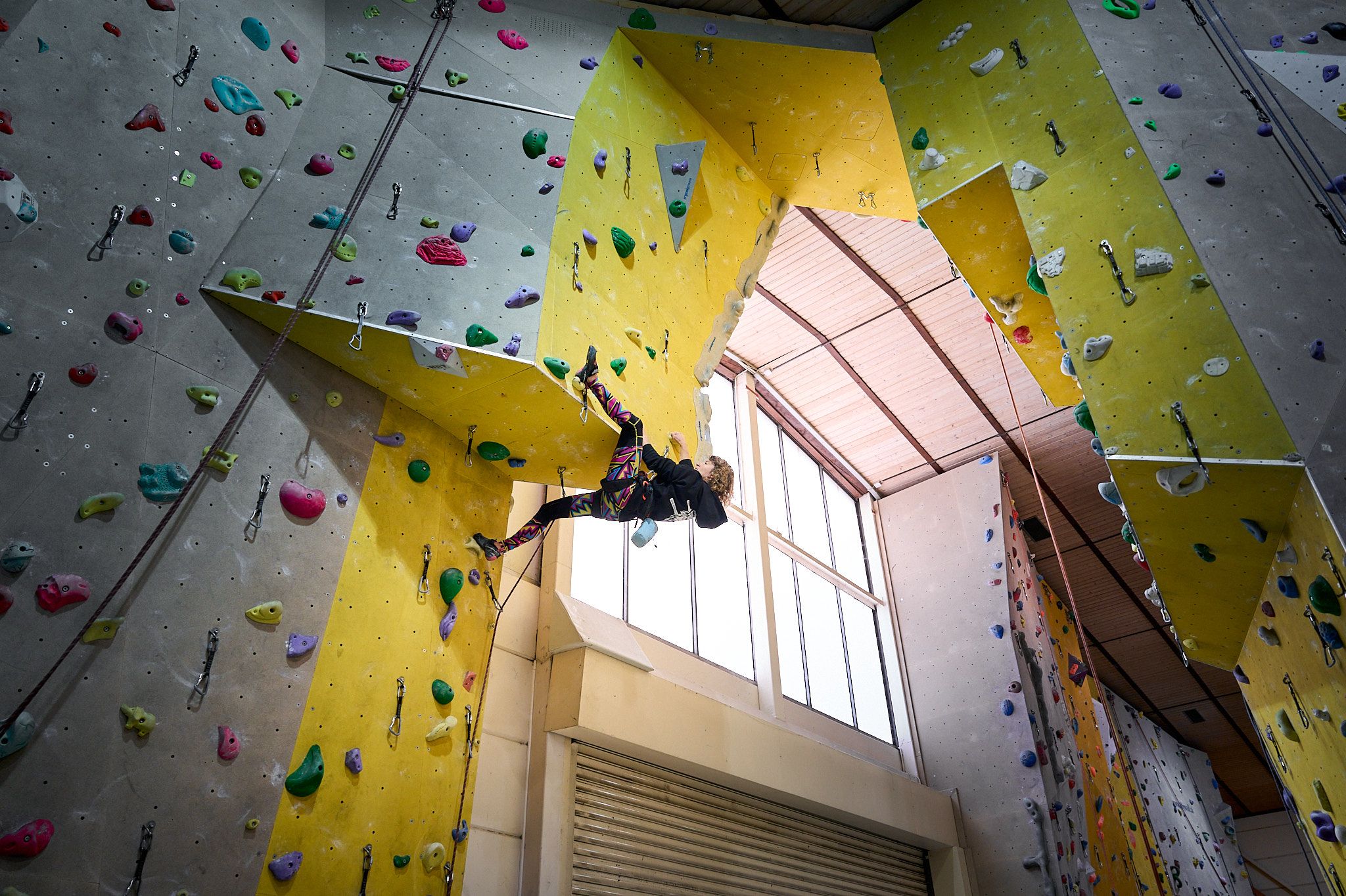 Person klettert an einer Indoor-Kletterwand mit bunten Griffen.