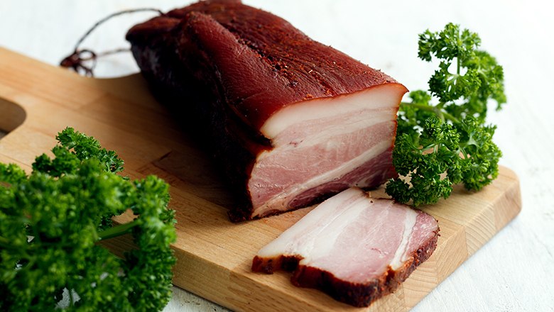 Ein St&uuml;ck Speck auf einem Holzbrett mit Petersilie.