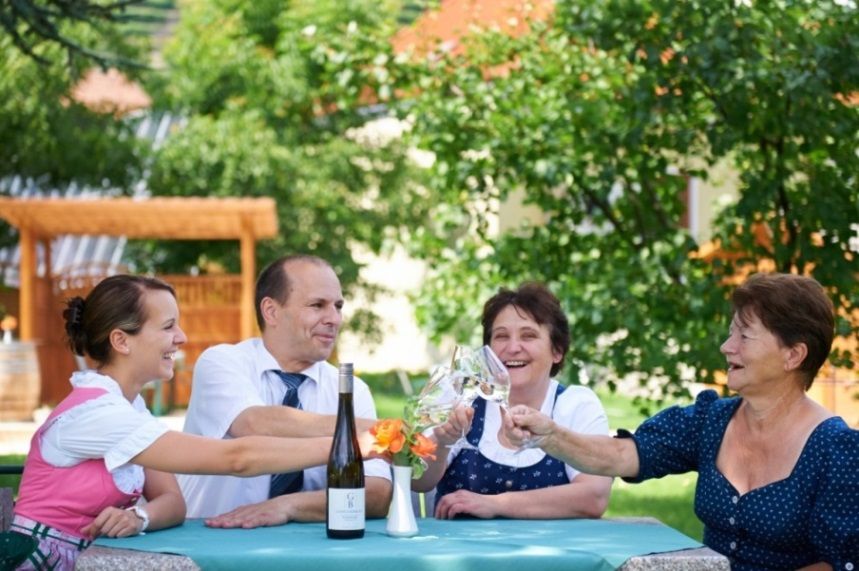 Vier Personen stoßen im Freien mit Weingläsern an.