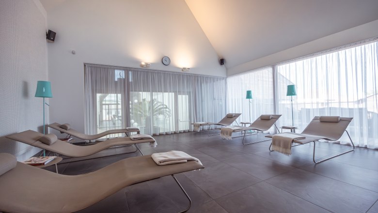 Ein heller Entspannungsraum mit Liegestühlen und Vorhängen.