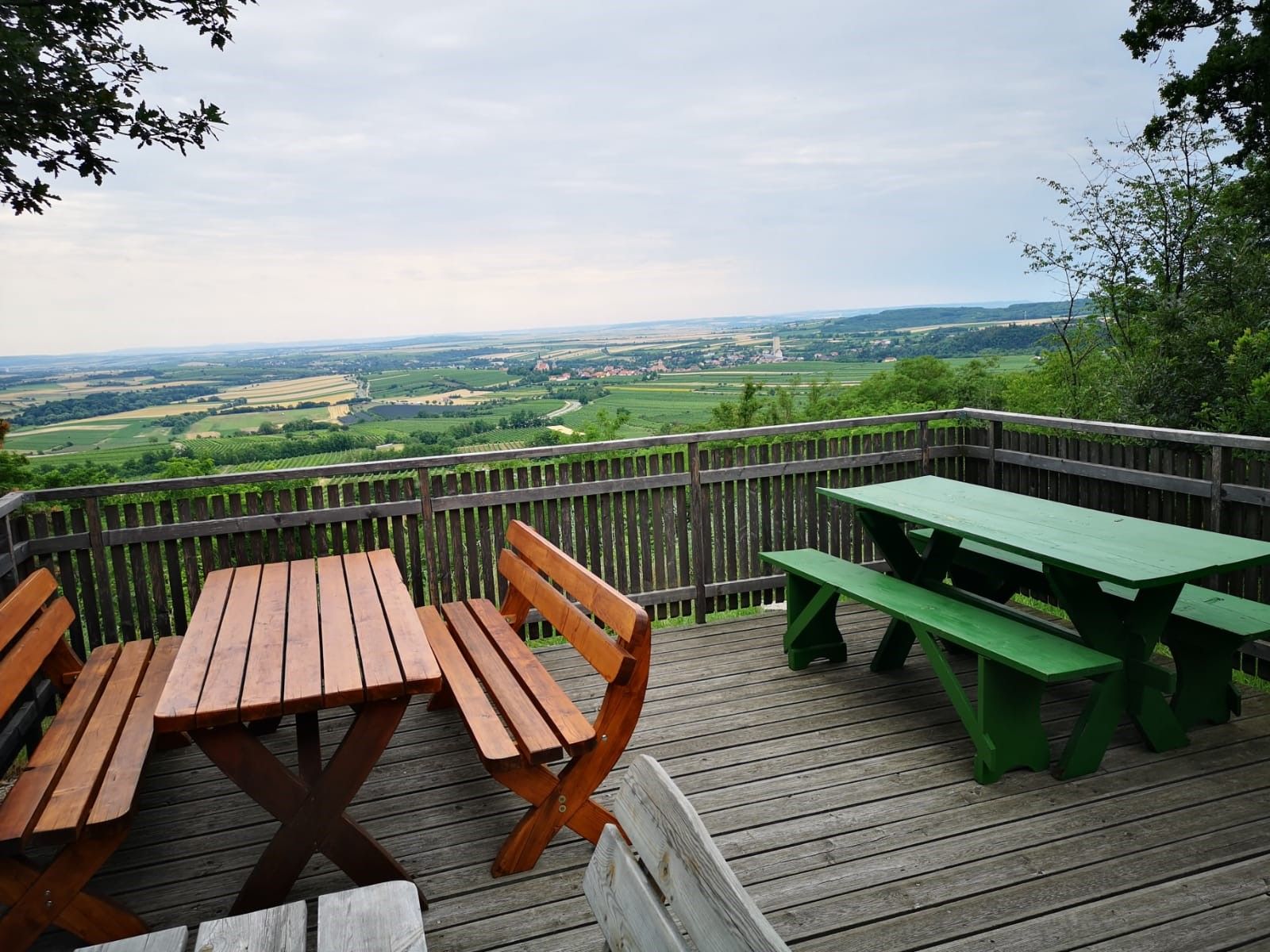 Aussichtsplattform mit Holzbänken und Tischen, Blick auf weite Landschaft und Felder.