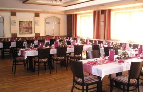 Ein elegant gedeckter Speisesaal mit mehreren Tischen, roten Tischläufern und Stühlen.