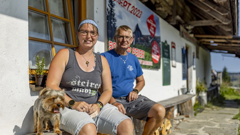 Zwei Personen sitzen vor einem Gebäude mit einem Hund, im Hintergrund ein Plakat mit Datum 09. Sept. 2023.