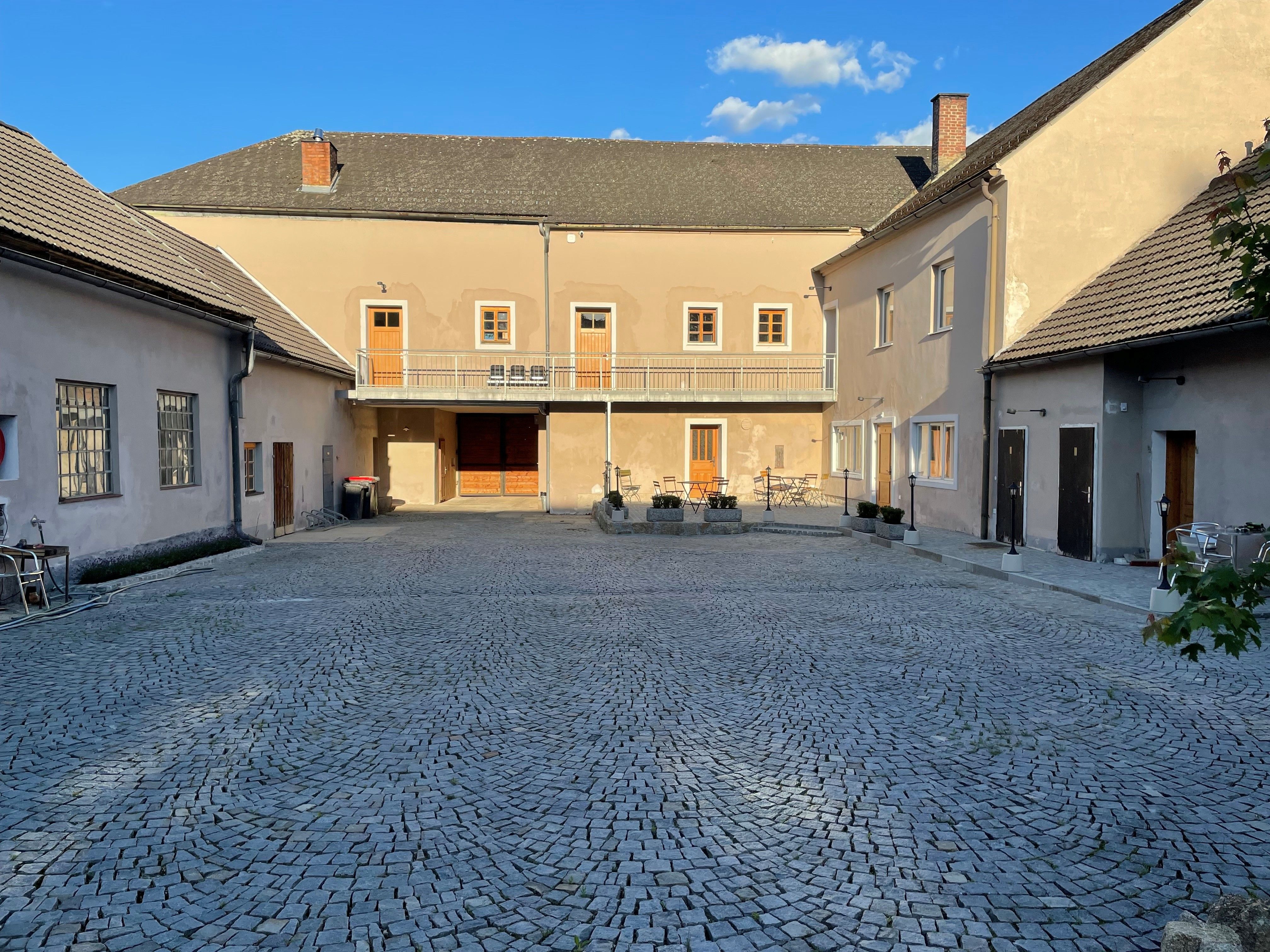 Ein gepflasterter Innenhof mit umgebenden Gebäuden und einem blauen Himmel im Hintergrund.