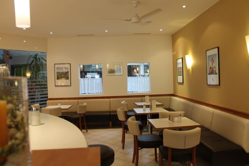 Innenansicht eines Cafés mit Tischen, Stühlen und Wanddekorationen.