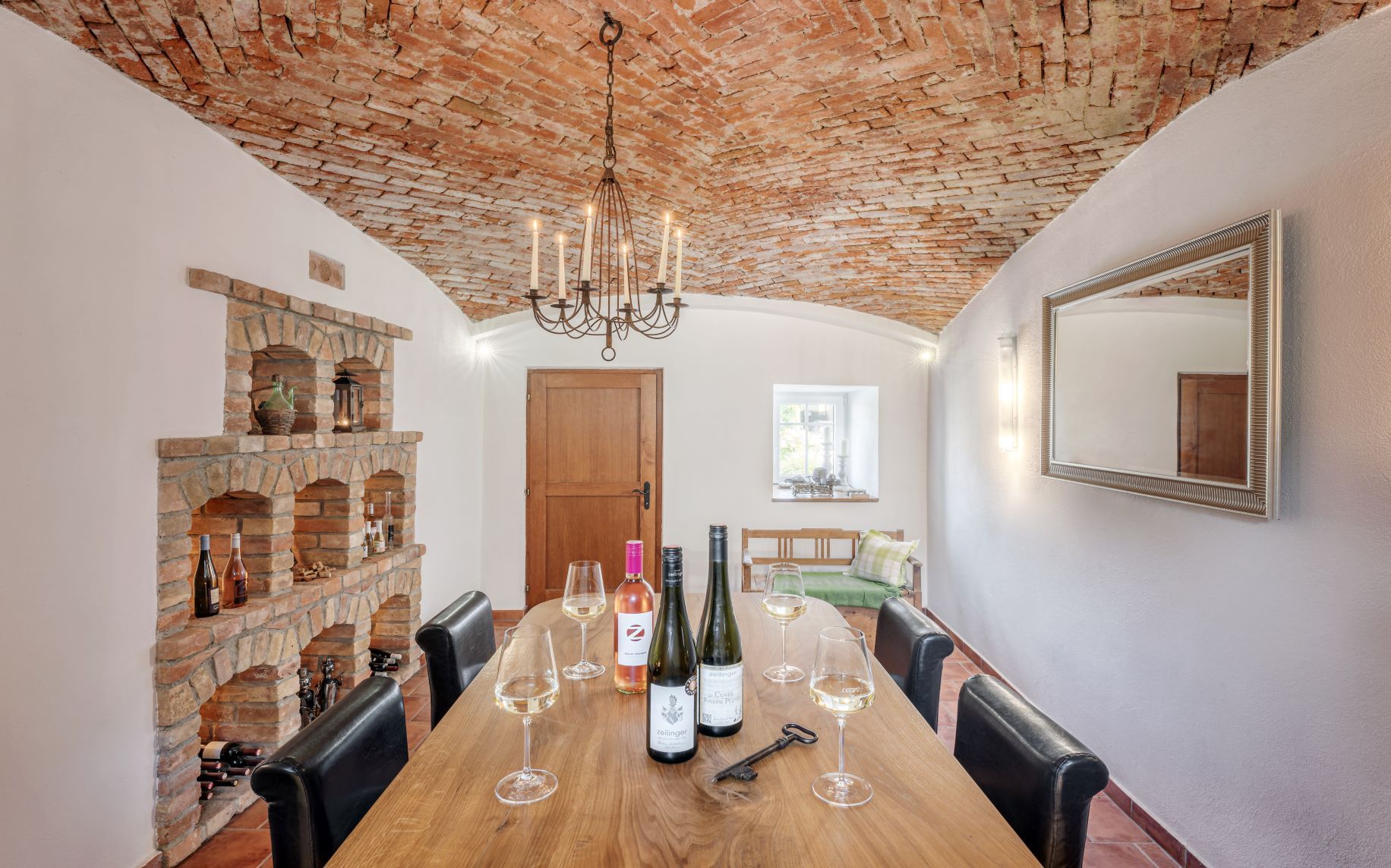 Gemütlicher Weinkeller mit Ziegelgewölbe, Holztisch, Weingläsern und Flaschen.