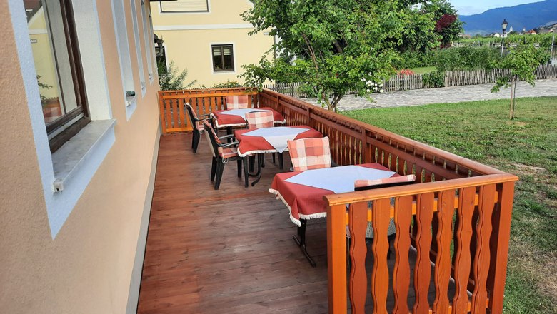 Holzterrasse mit gedeckten Tischen und St&uuml;hlen, umgeben von gr&uuml;ner Landschaft.