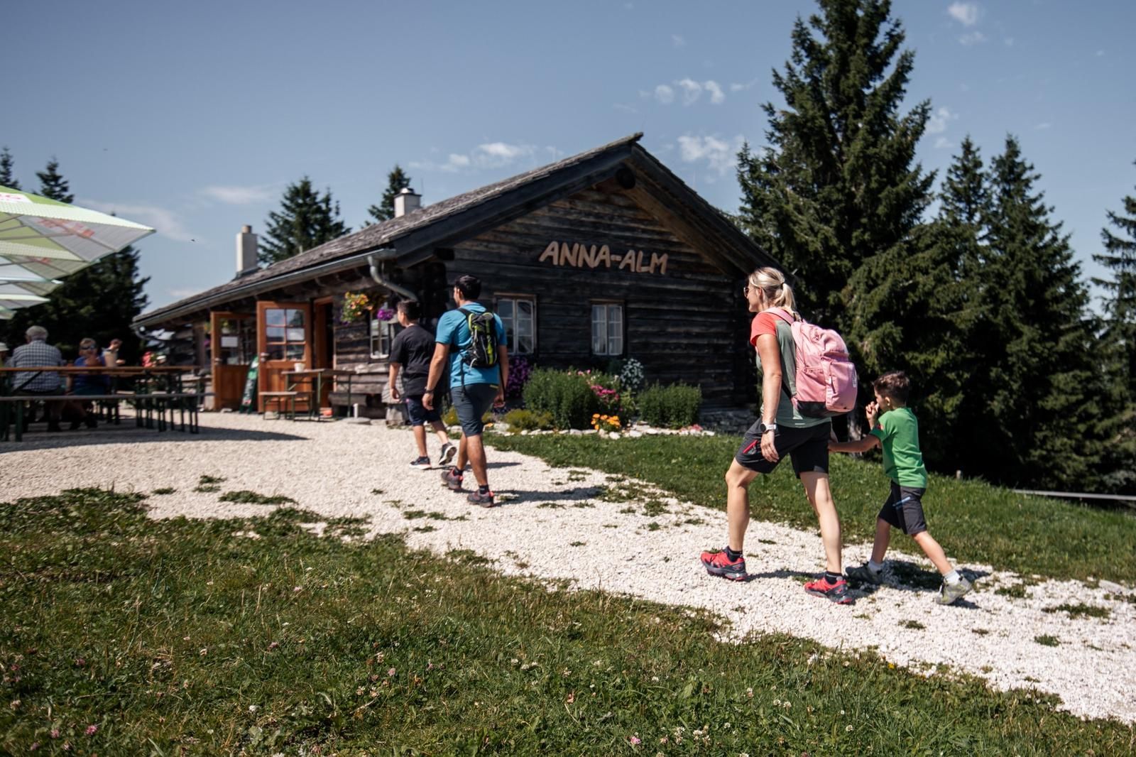 Wandernde Familien und Ausflugsgäste erreichen die gemütliche Anna-Alm inmitten der Berglandschaft – ein beliebter Einkehrort mit uriger Hüttenatmosphäre.