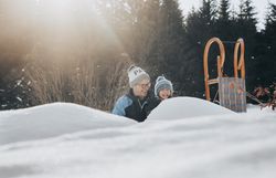 Eine fröhliche Familie genießt den Winter in der verschneiten Landschaft der Ybbstaler Alpen. Lachen und Freude erfüllen die Luft, während sie gemeinsam mit einem Schlitten die sanften Hügel hinunterrodeln. Die strahlende Sonne und der glitzernde Schnee schaffen eine magische Atmosphäre.