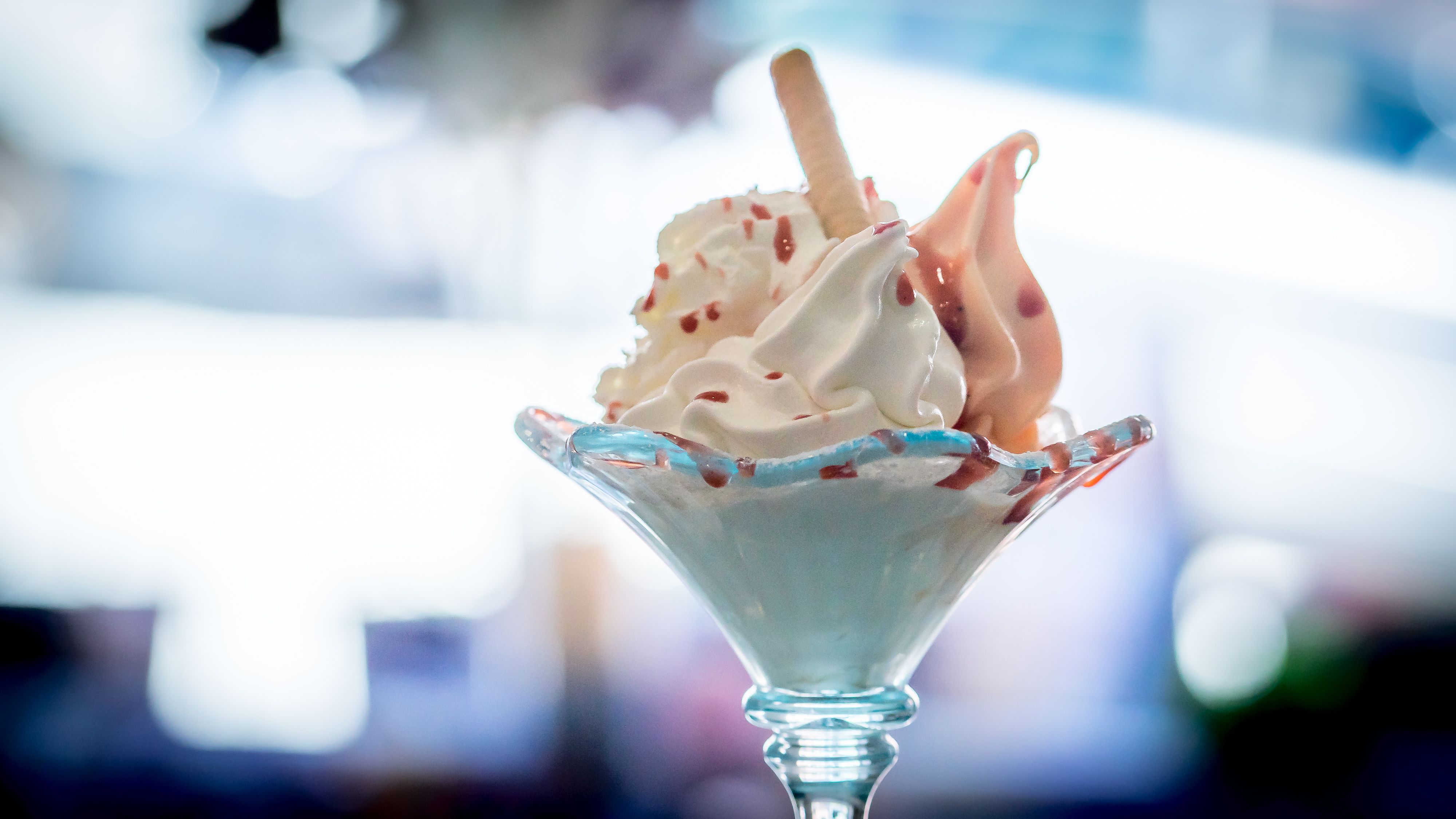 Ein Eisbecher mit Sahne und Soße in einem Glas auf unscharfem Hintergrund.