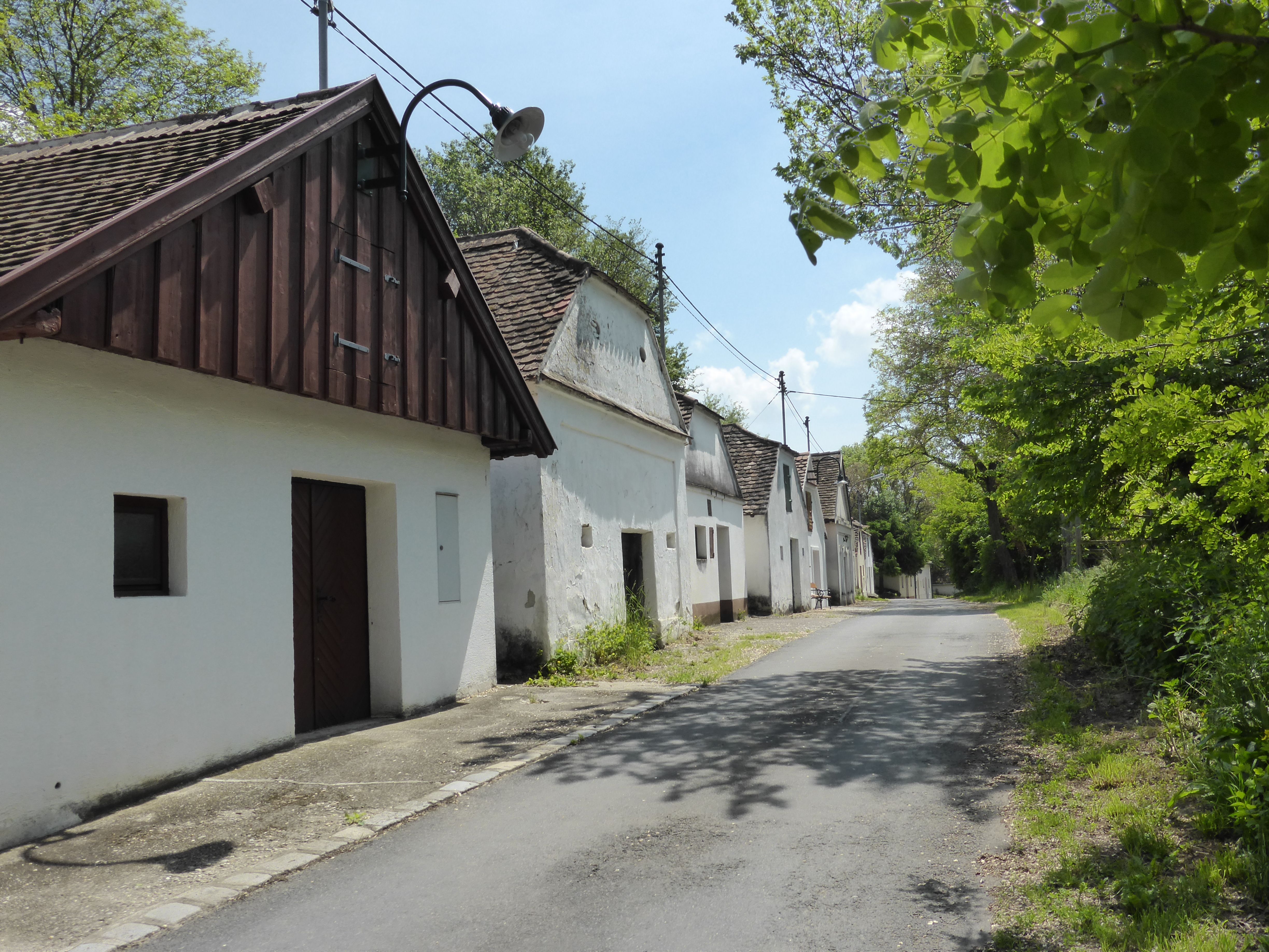 Reihe von traditionellen weißen Häusern entlang einer ruhigen Straße, umgeben von Bäumen und grünem Laub.