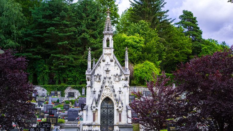 Eine gotische Grabkapelle auf einem Friedhof, umgeben von Bäumen und Grabsteinen.