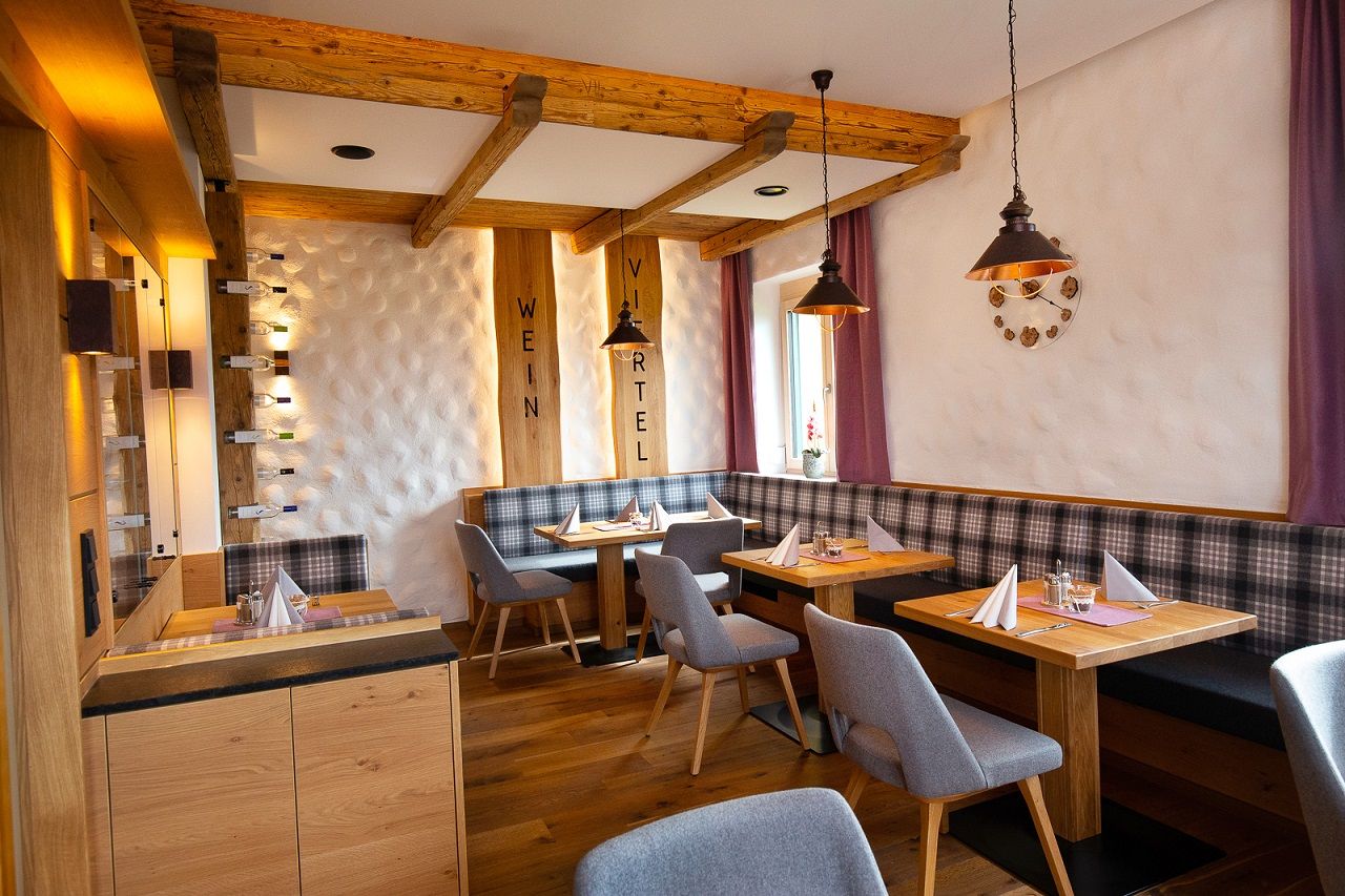Gemütliches Restaurant mit Holzmöbeln, gedeckten Tischen und lila Vorhängen.