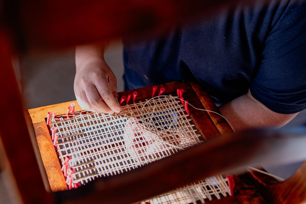 Eine Person repariert ein Thonet Stuhl mit Wiener Geflecht.