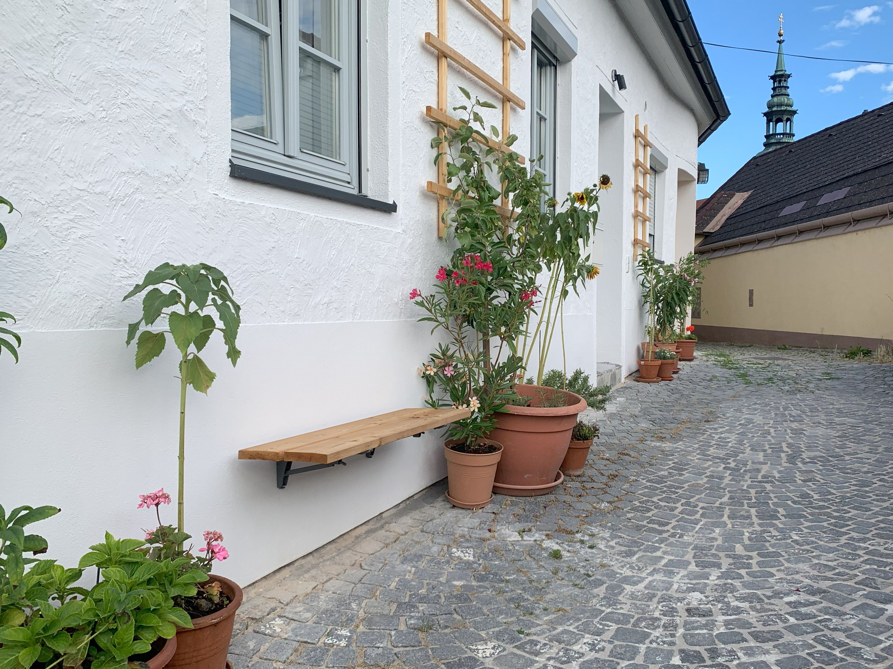Gepflasterter Weg mit Topfpflanzen vor einem weißen Gebäude.