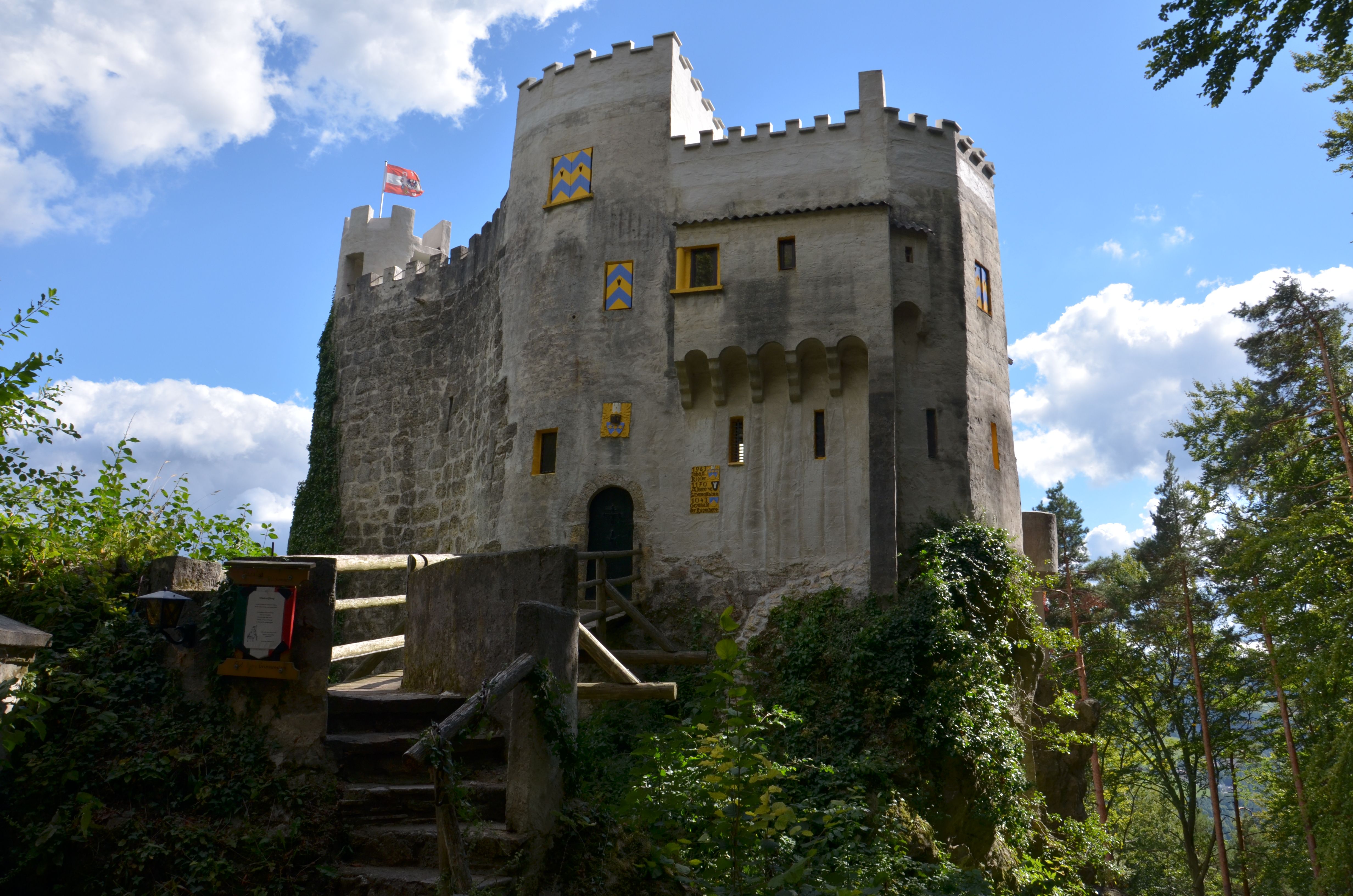 Burg Grimmenstein mit Brücke, Zinnen und blau-gelb gestrichenen Fensterläden im Grünen.