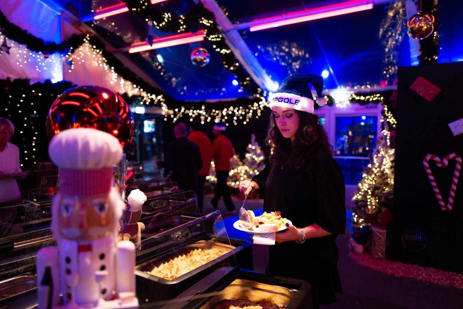 Stimmungsvoll beleuchtetes Winterevent bei Topgolf mit festlicher Dekoration, Weihnachtslichtern und Buffet in gemütlicher Weihnachtsatmosphäre.