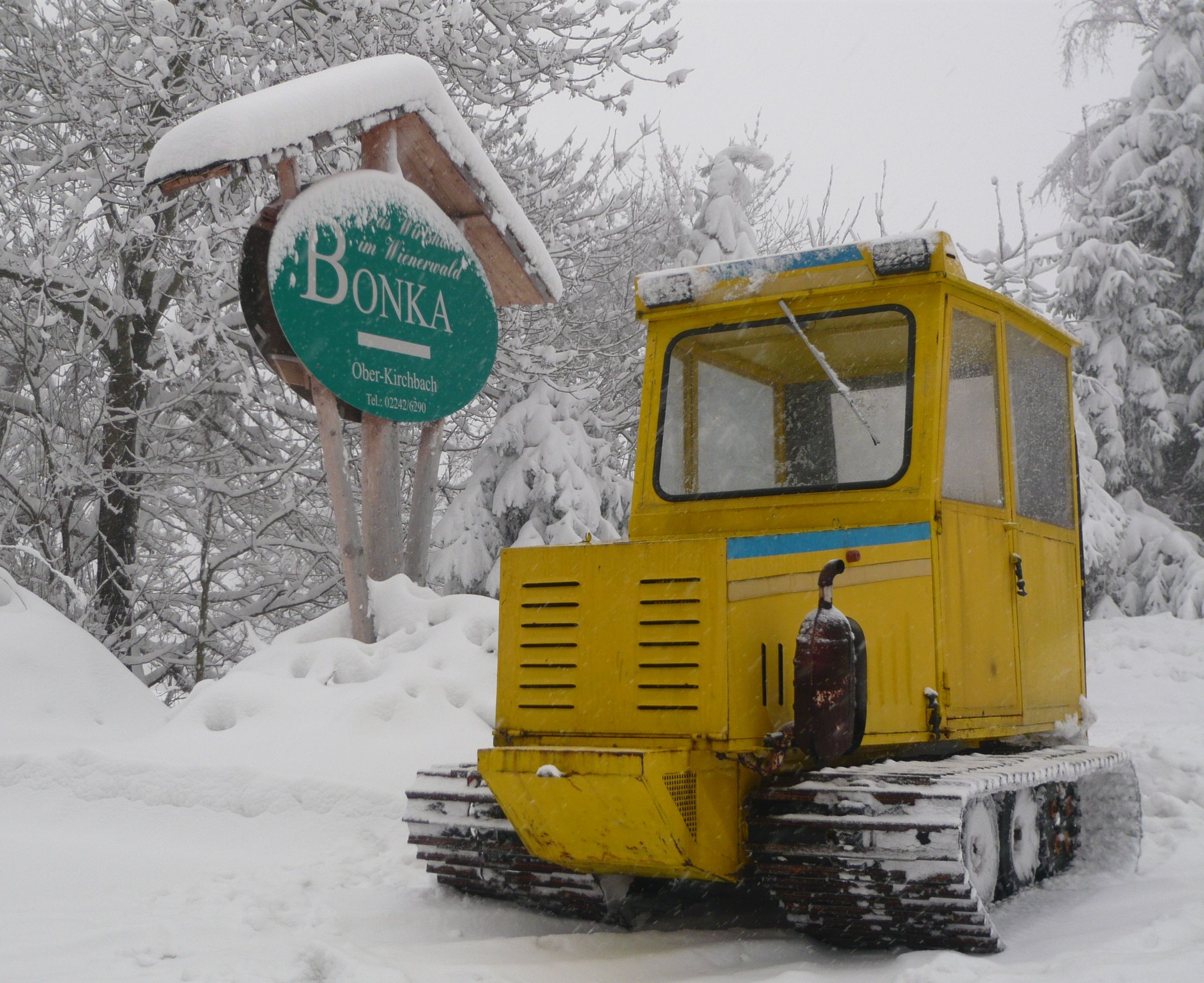 Gelbes Schneefahrzeug im Schnee vor einem Schild mit der Aufschrift 'Bonka' in Oberkirchbach.